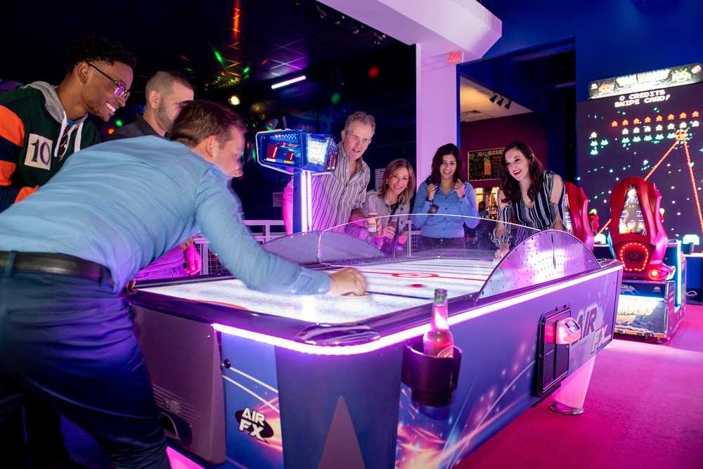 A group of people enjoying air hockey in an arcade during Things to Do in Miami at Night.