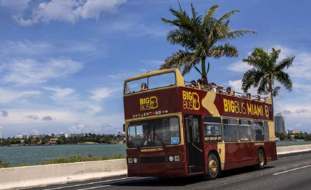 Attractions in downtown Miami: A double decker bus driving down the road at night with palm trees in the background, showcasing Miami's vibrant nightlife.