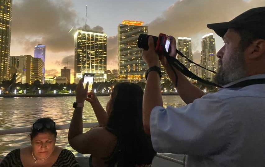 A group of people on a boat capturing the Miami skyline during a night event.