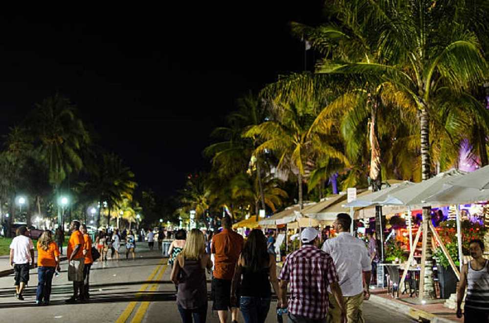 Nightlife in Miami: People strolling under palm trees on a bustling street.