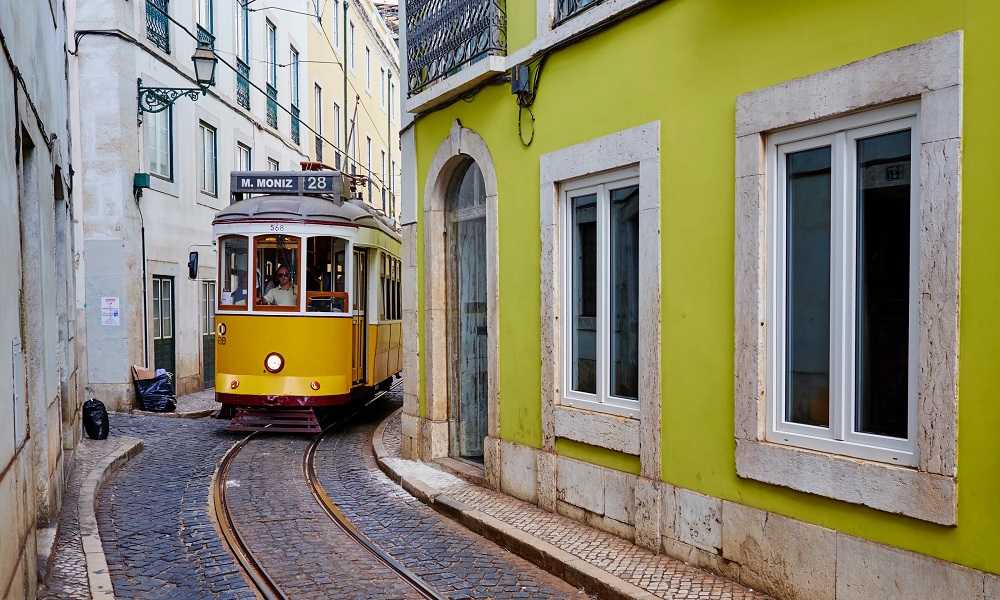 Best things to do in Lisbon: A yellow tram 28 traveling down a narrow street.
