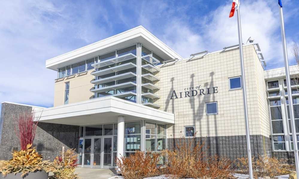 Modern municipal building, among the best places to live in Alberta, with the sign "city of Airdrie" under a blue sky.
