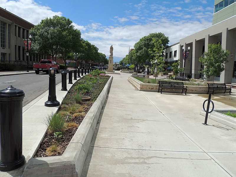 Urban street with benches, a statue in the distance, and a landscaped pedestrian path showcasing one of the best places to live in Alberta.
