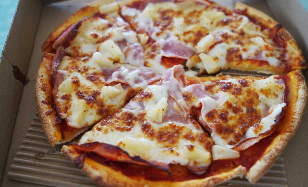 A pizza in a cardboard box with cheese and ham, reminiscent of the Canadian Rockies.