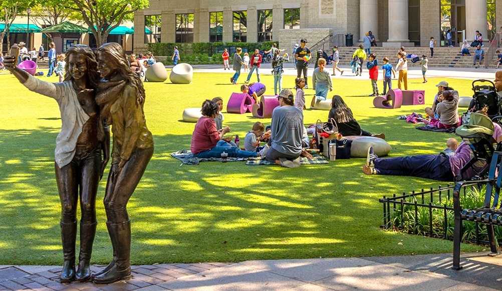 Sugarland, TX: A group of people sitting on the grass in one of the safest cities in America, in front of a statue.