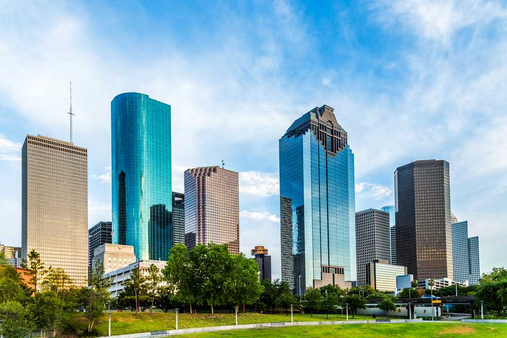 A cityscape featuring modern high-rise buildings with Buffalo Bayou Park in the foreground under a blue sky with light clouds, showcasing one of the best things to do in Houston.