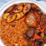 A white plate containing jollof rice, fried plantains, and stewed meat with vegetables, just like the delightful offerings you'd find at one of the best African restaurants in Houston.