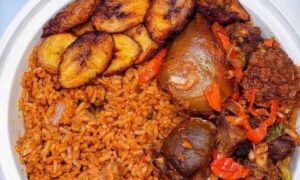 A white plate containing jollof rice, fried plantains, and stewed meat with vegetables, just like the delightful offerings you'd find at one of the best African restaurants in Houston.