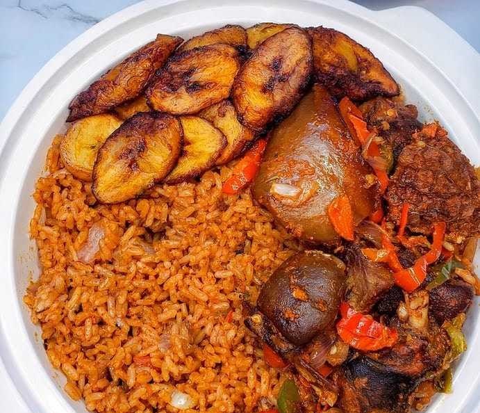 A white plate containing jollof rice, fried plantains, and stewed meat with vegetables, just like the delightful offerings you'd find at one of the best African restaurants in Houston.